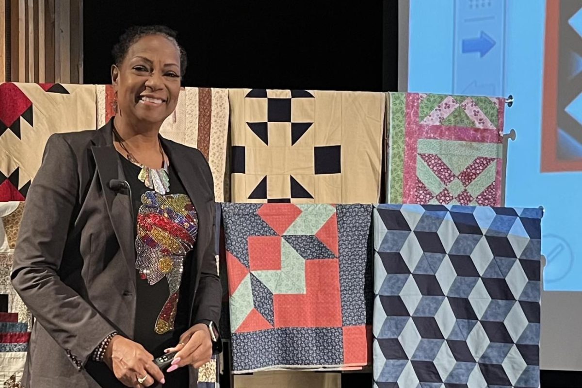 Connie Martin poses in front of a display of her quilts in the J Theatre (J143) on February 28th. (Photo by Tori Malek)